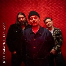 Drei Männer posieren vor einer roten Wand.