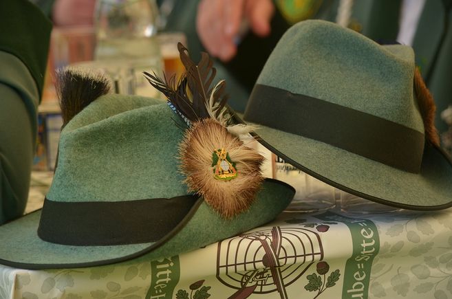 Zwei grüne Hüte mit Federn und Abzeichen auf einem Tisch beim Schützenfest.