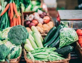 Frisches Gemüse auf einem Wochenmarkt, darunter Brokkoli, Karotten, Zucchini und Tomaten.