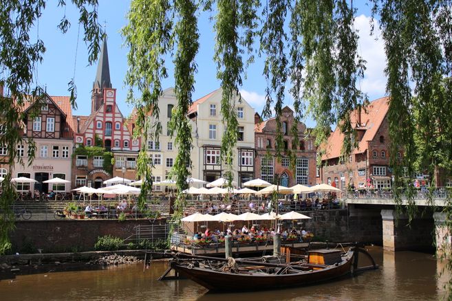 Historische Gebäude und Cafés an einem Flussufer mit einem alten Boot im Vordergrund.
