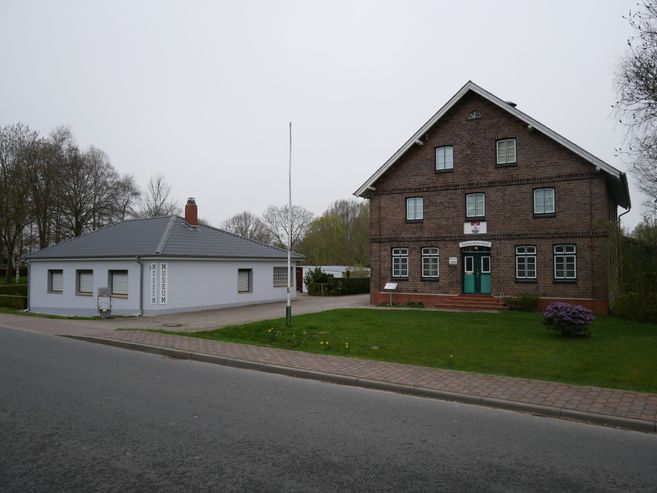 Ein kleines Museum und ein größeres Backsteingebäude an einer Straße.
