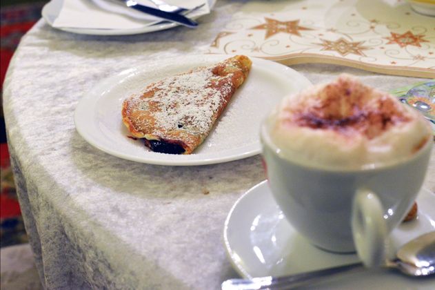Ein Teller mit einem Pfannkuchen und eine Tasse Cappuccino auf einem Tisch.