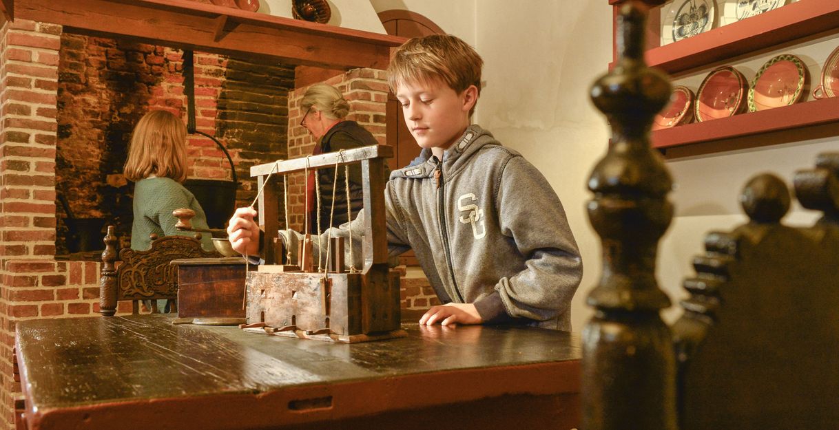 Ein Junge spielt mit einem alten Spielzeug in einem historischen Raum mit Kamin und antikem Geschirr.