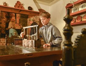 Ein Junge spielt mit einem alten Spielzeug in einem historischen Raum mit Kamin und antikem Geschirr.