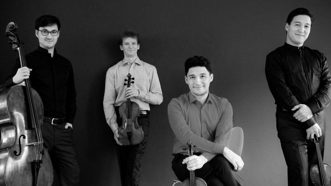 Vier Musiker des Schumann Quartetts posieren mit ihren Instrumenten vor einem dunklen Hintergrund.