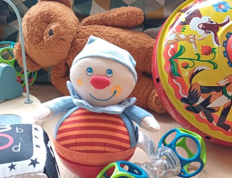 Spielzeug und Kuscheltiere in einer Krabbelgruppe: ein Stoffclown, ein Teddybär und buntes Babyspielzeug auf dem Boden.