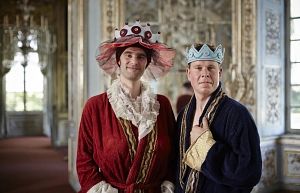 Zwei Männer in königlichen Gewändern und Kronen stehen in einem prunkvollen Raum.