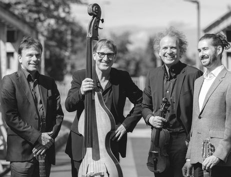 Vier Männer mit Musikinstrumenten auf einer Brücke.