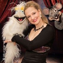 Eine Frau mit einer weißen Vogel-Handpuppe und einer grauen Maus-Puppe im Hintergrund.