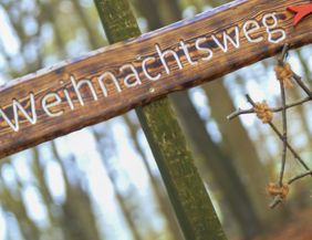 Holzschild mit der Aufschrift 'Weihnachtsweg' im Wald.