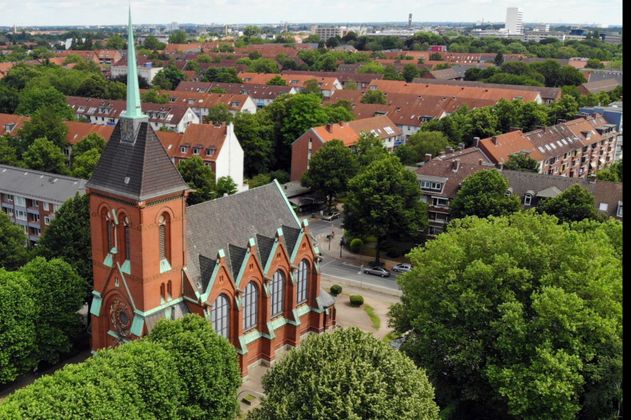 Luftaufnahme einer Kirche inmitten einer Wohngegend mit vielen Bäumen.