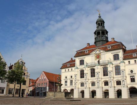 Historisches Rathaus mit Turm und umliegenden Gebäuden auf einem Platz bei klarem Himmel.