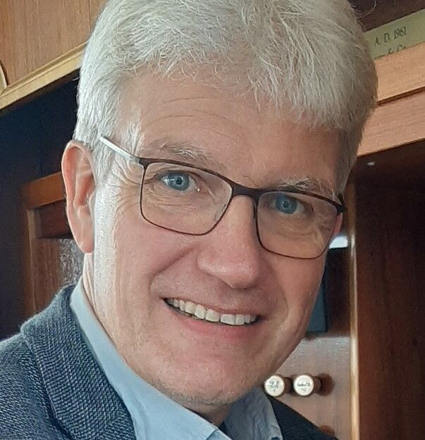 Porträt eines lächelnden Mannes mit Brille und grauem Haar.