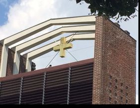 Nahaufnahme eines Kirchturms mit einem goldenen Kreuz auf einem Backsteingebäude.