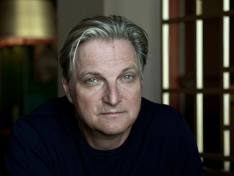 Porträt eines Mannes mit grauem Haar und dunklem Pullover in einem Innenraum.