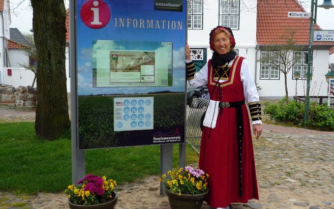 Eine Frau in traditioneller Kleidung steht neben einem Informationsschild in Wesselburen.