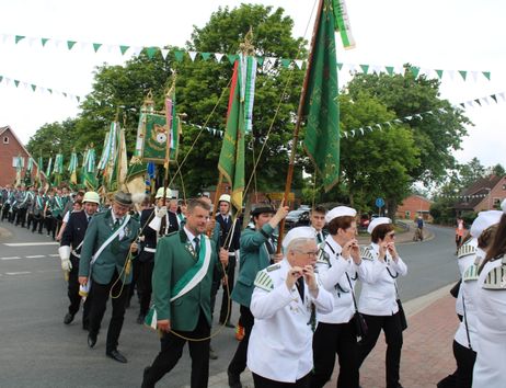 Menschen in grünen Uniformen und weißen Hemden marschieren mit Fahnen bei einem Schützenfest.