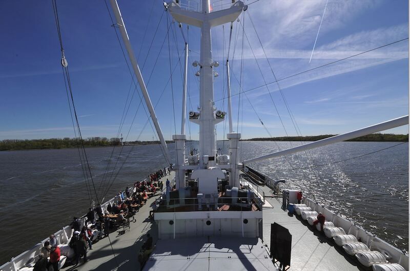 Blick vom Deck eines Schiffes auf der Elbe, mit Passagieren und blauem Himmel.