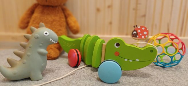 Spielzeug im Eltern-Kind-Treff / Krabbelgruppe: grünes Krokodil, grauer Dino, bunte Greifkugel und Teddybär im Hintergrund.