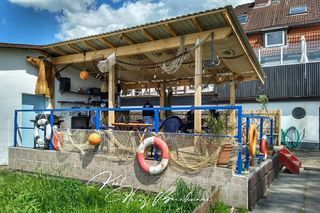Überdachte Terrasse mit maritimer Dekoration, Rettungsringen und Fischernetzen.