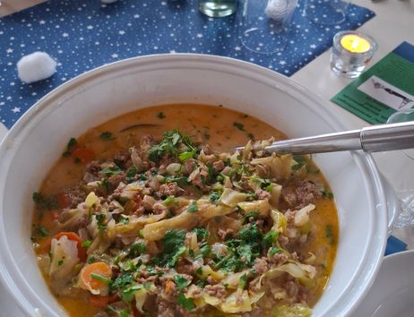 Ein Tisch mit einer großen Schüssel Eintopf, umgeben von Tellern, Gläsern und einer Kerze.