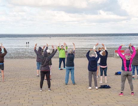 Gruppe von Menschen macht Qi Gong-Übungen am Strand mit Blick auf das Meer.