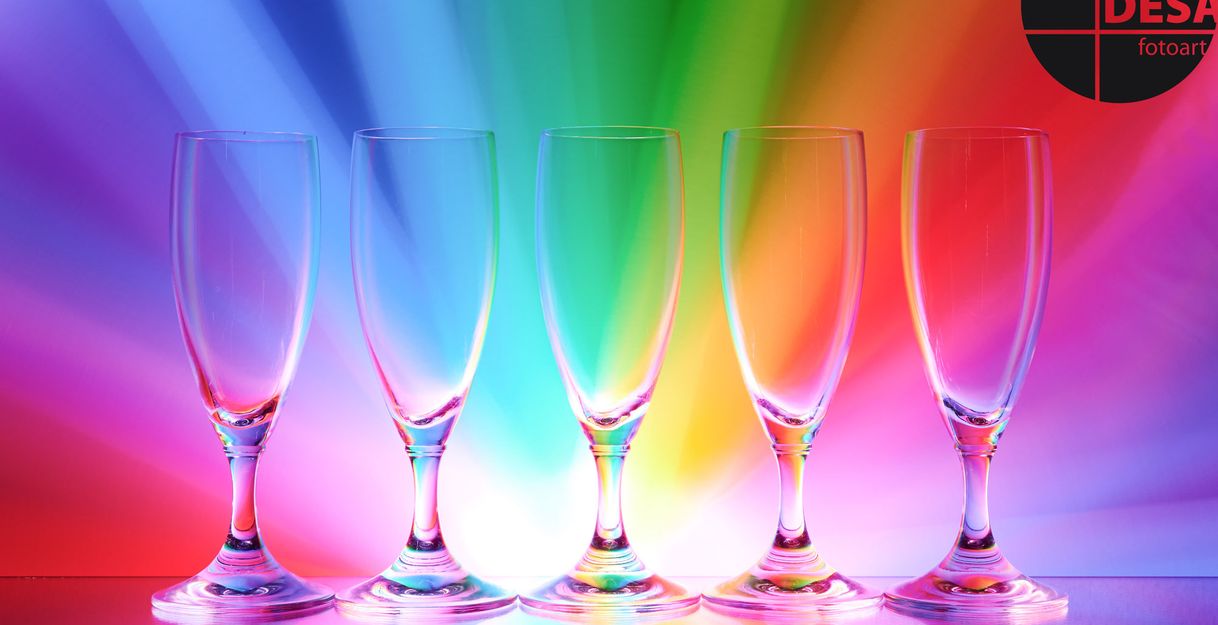 Fünf leere Sektgläser vor einem bunten, regenbogenfarbenen Hintergrund.