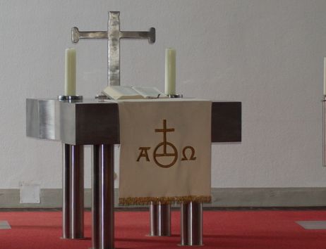 Ein moderner Altar mit einem Kreuz, Kerzen und einem Tuch mit christlichen Symbolen.