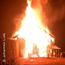 Ein brennendes Haus bei Nacht mit großen Flammen, die aus dem Dach schlagen.