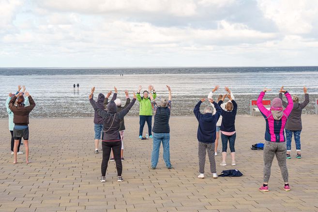 Gruppe von Menschen macht Qi Gong-Übungen am Strand mit Blick auf das Meer.