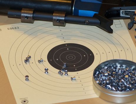 Zielscheibe mit Luftgewehr und Diabolos auf einem Tisch.