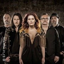 Eine Musikgruppe mit fünf Mitgliedern posiert vor einem dunklen Hintergrund.