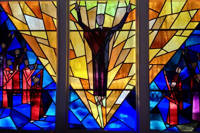 Buntes Kirchenfenster mit abstrakten Figuren und leuchtenden Farben.