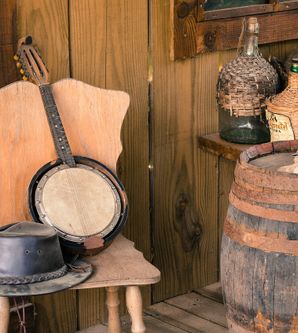 Banjo und Hut auf einem Stuhl. Daneben ein altes Fass und große Flaschen