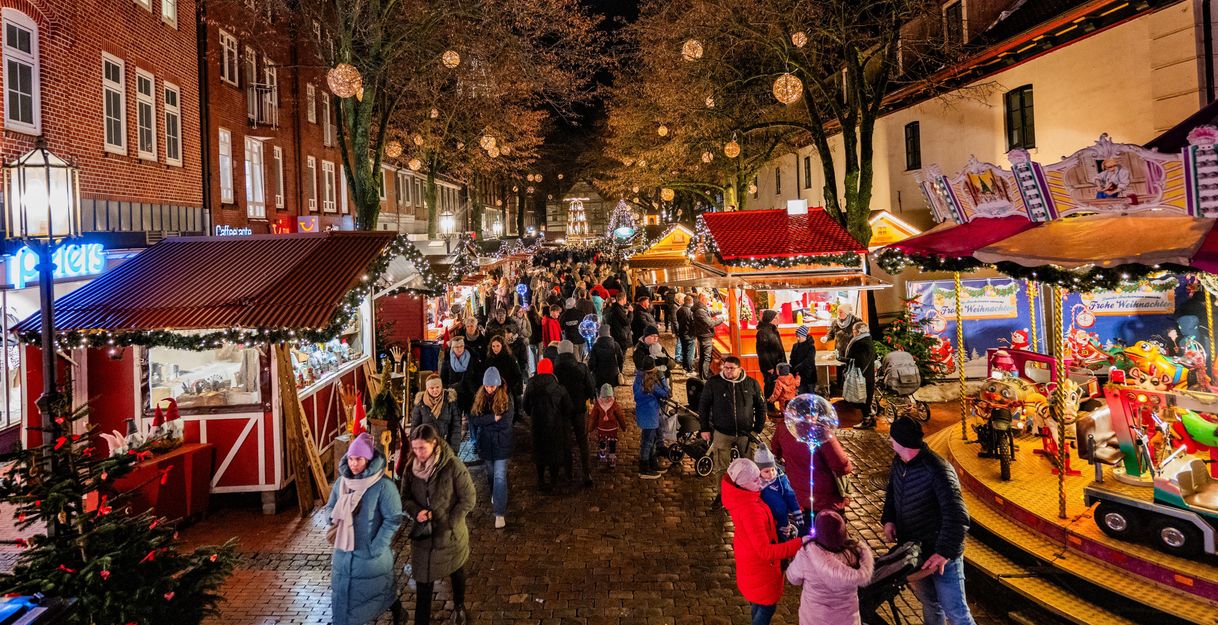 Menschenmenge auf dem Stader Weihnachtsmarkt mit beleuchteten Ständen und Karussell.
