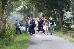 Eine Gruppe von Menschen steht auf einem schmalen Weg im Freien, umgeben von Bäumen und Gras.