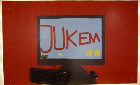 Wandgemälde mit einem Computerbildschirm, auf dem "JuKeM" steht, darunter eine Tastatur und Maus.