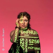 Eine Person vor einem rosa Hintergrund mit leuchtenden Zahlen und Wörtern auf dem Körper projiziert.