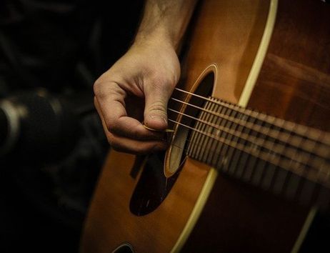 Nahaufnahme einer Hand, die eine Akustikgitarre spielt.