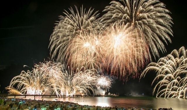 Ein großes Feuerwerk erleuchtet den Nachthimmel über der Ostsee, während Menschen am Strand zuschauen.