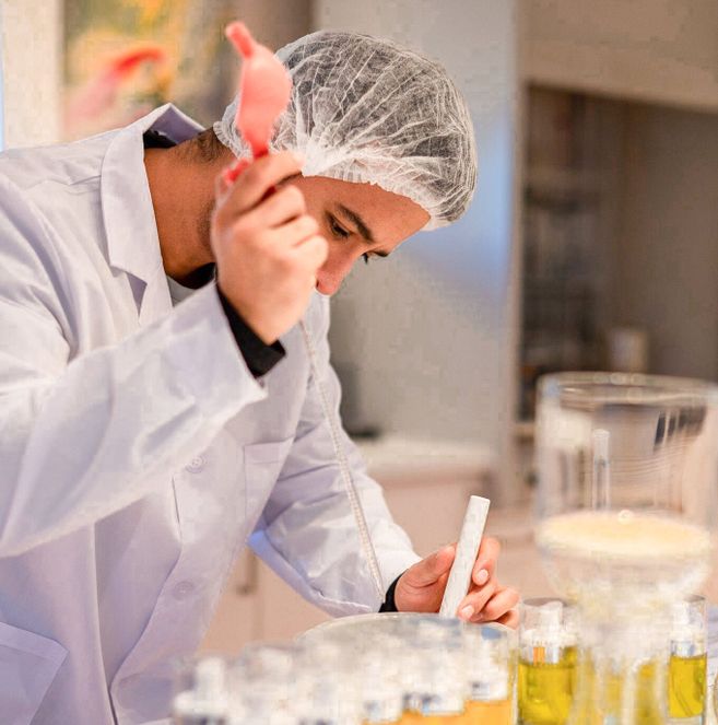 Person in weißem Laborkittel und Haarnetz arbeitet mit Laborgeräten und Flüssigkeiten.