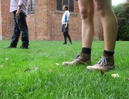 Drei Personen stehen auf einer grünen Wiese vor einem Backsteingebäude.