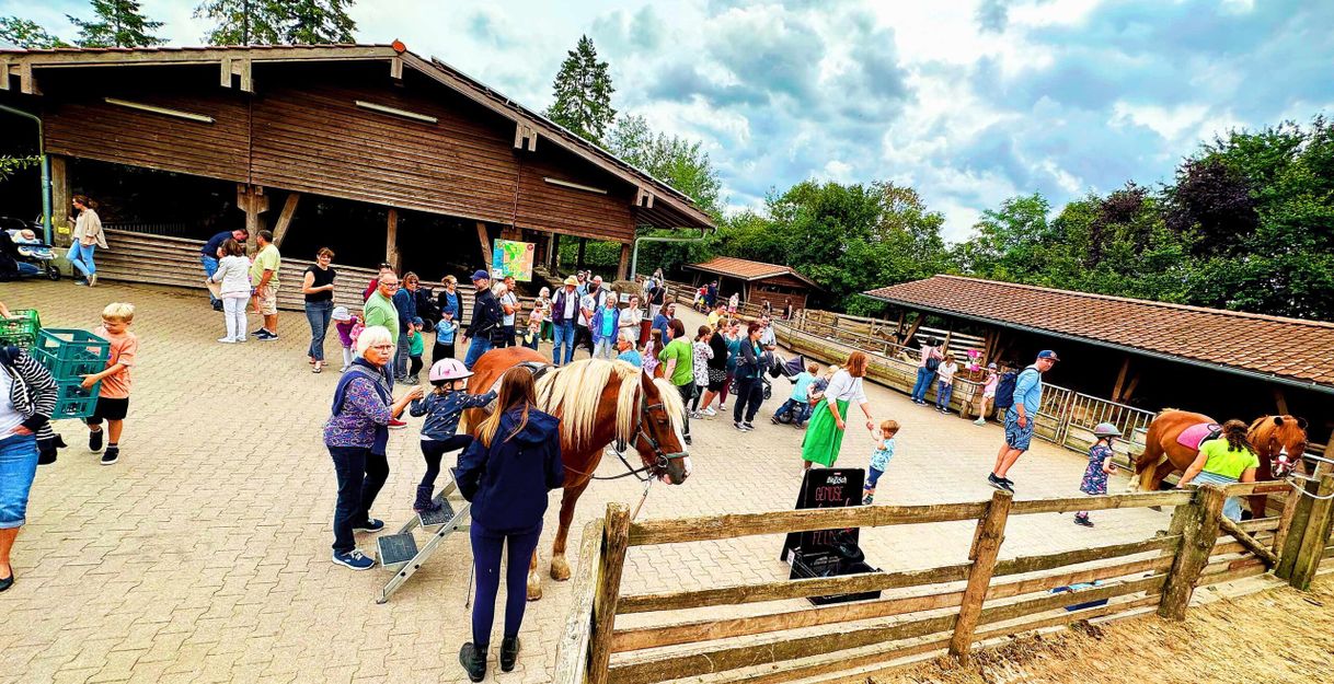 Menschen auf einem Bauernhof mit Pferden und Ställen im Hintergrund.