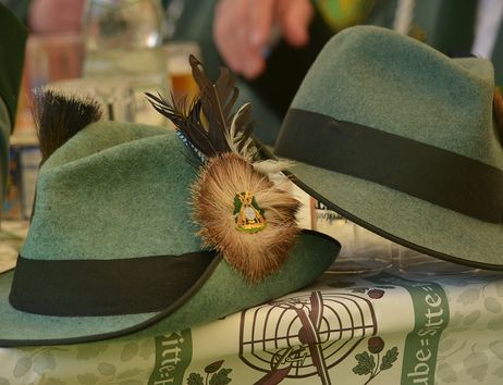 Zwei grüne Hüte mit Federn und Abzeichen auf einem Tisch beim Schützenfest.
