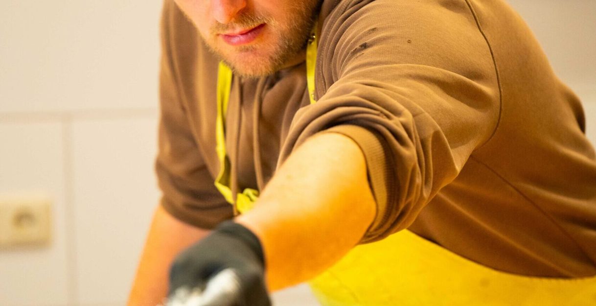 Ein Mann in einer Bäckerschürze streut Mehl auf eine Arbeitsfläche.