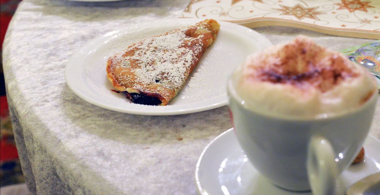 Ein Teller mit einem Pfannkuchen und eine Tasse Cappuccino auf einem Tisch.