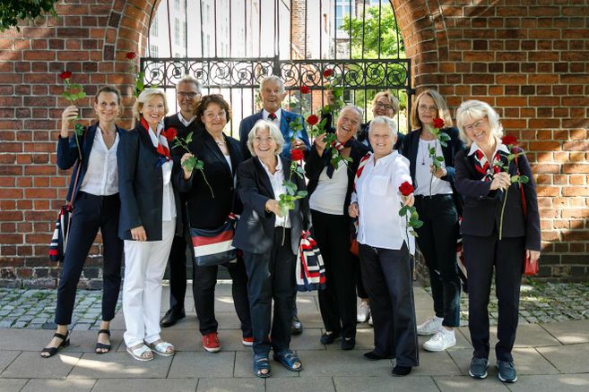 Eine Gruppe von Menschen hält rote Rosen vor einem Backsteinbogen.