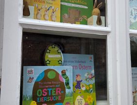 Ein Schaufenster mit Osterbüchern und Dekorationen, darunter Plüschhasen und bunte Kinderbücher.