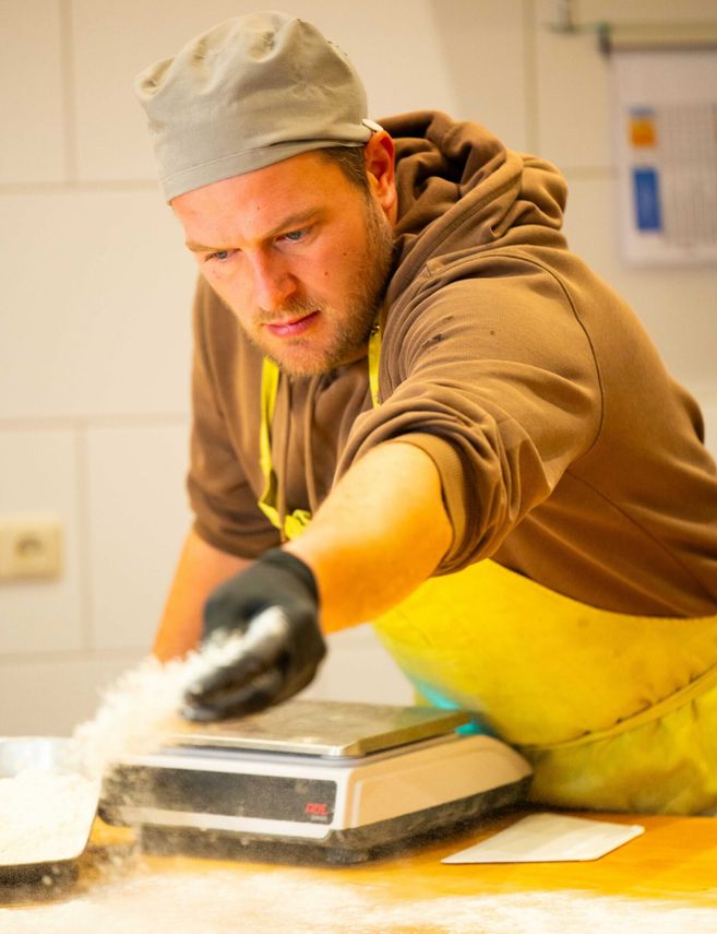 Ein Mann in einer Bäckerschürze streut Mehl auf eine Arbeitsfläche.