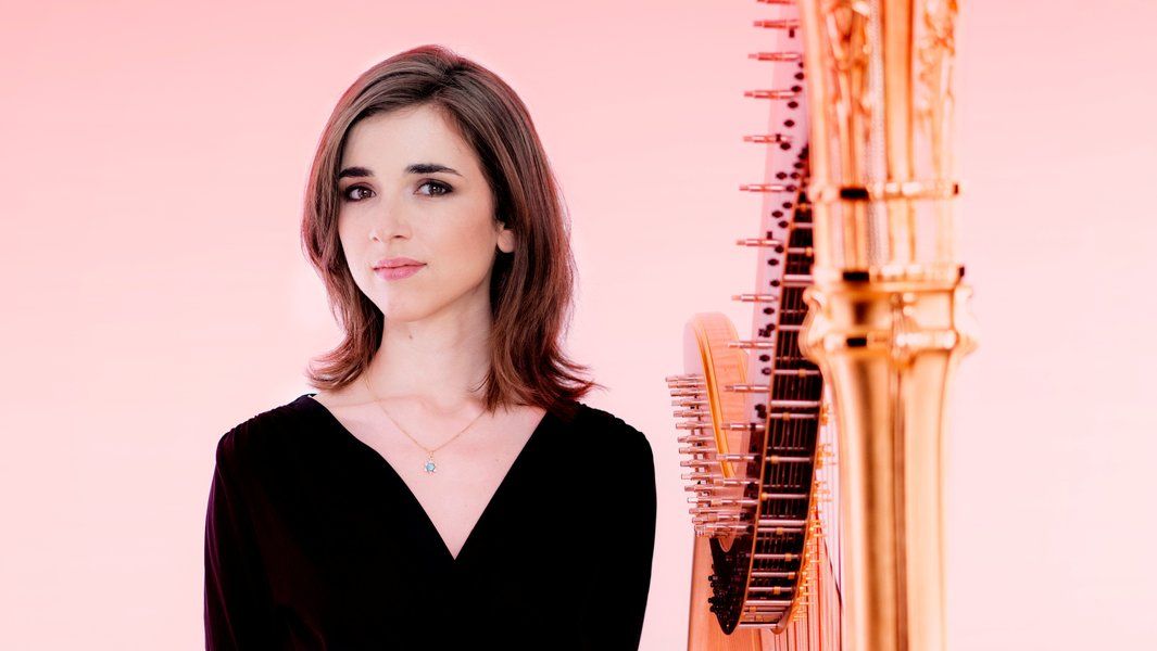 Eine Frau steht neben einer Harfe vor einem rosa Hintergrund.